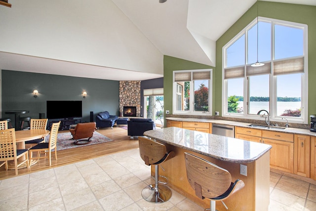 kitchen with sink, light stone countertops, stainless steel dishwasher, a water view, and light brown cabinets