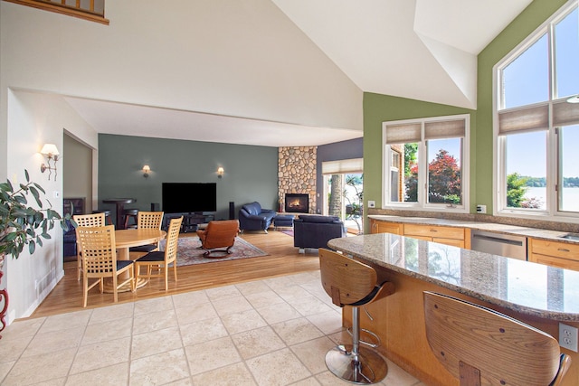 kitchen featuring light stone counters, high vaulted ceiling, a fireplace, and stainless steel dishwasher