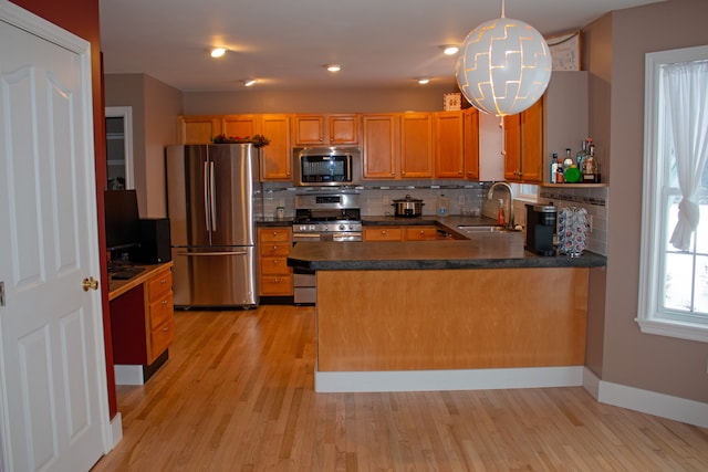 kitchen featuring stainless steel appliances, sink, light wood-type flooring, and decorative light fixtures