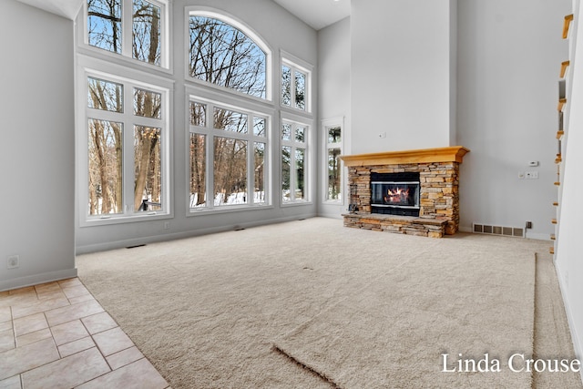 tiled living area with visible vents, a towering ceiling, carpet flooring, a stone fireplace, and baseboards