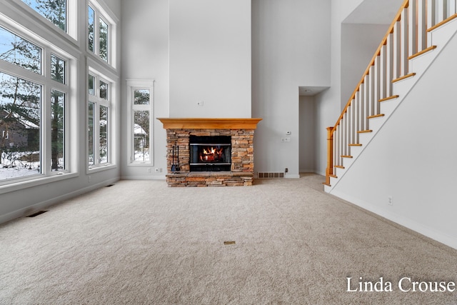 unfurnished living room with a fireplace, carpet flooring, a towering ceiling, visible vents, and stairs