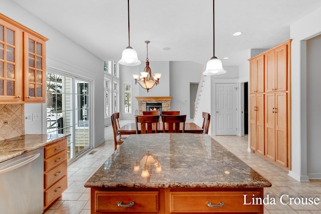 kitchen featuring dark stone counters, dishwasher, glass insert cabinets, decorative light fixtures, and a fireplace