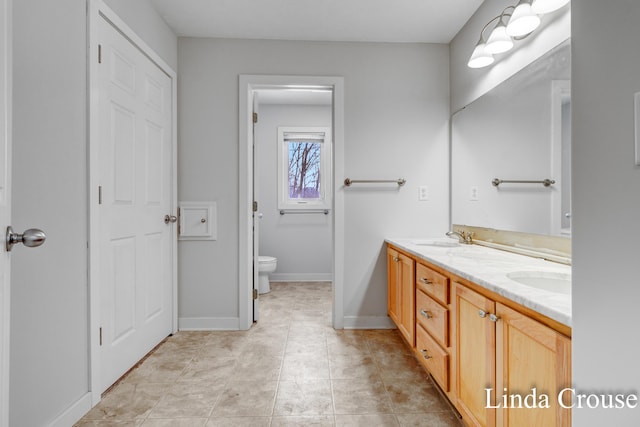 bathroom with toilet, double vanity, baseboards, and a sink