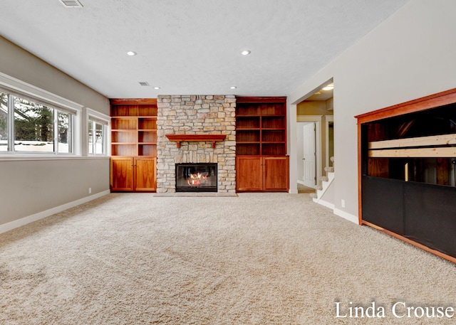 unfurnished living room with built in features, carpet flooring, a stone fireplace, a textured ceiling, and baseboards