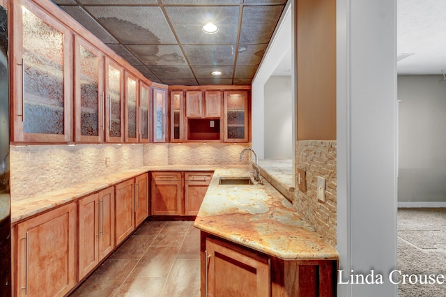 kitchen featuring glass insert cabinets, a sink, light stone countertops, backsplash, and recessed lighting