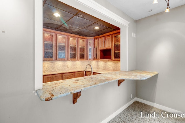 kitchen with decorative backsplash, a breakfast bar, glass insert cabinets, and baseboards