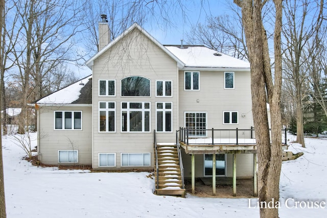 snow covered back of property with stairs, a chimney, and a deck