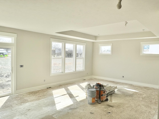 empty room with a raised ceiling, a healthy amount of sunlight, and baseboards