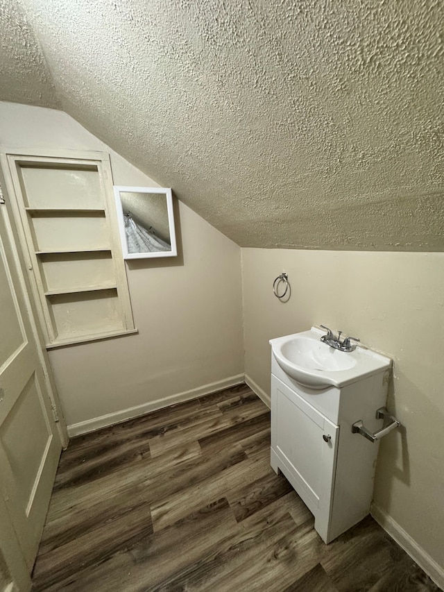 bathroom with vaulted ceiling, vanity, a textured ceiling, wood finished floors, and baseboards