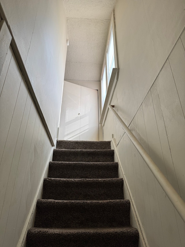 stairway with wood walls and a textured ceiling