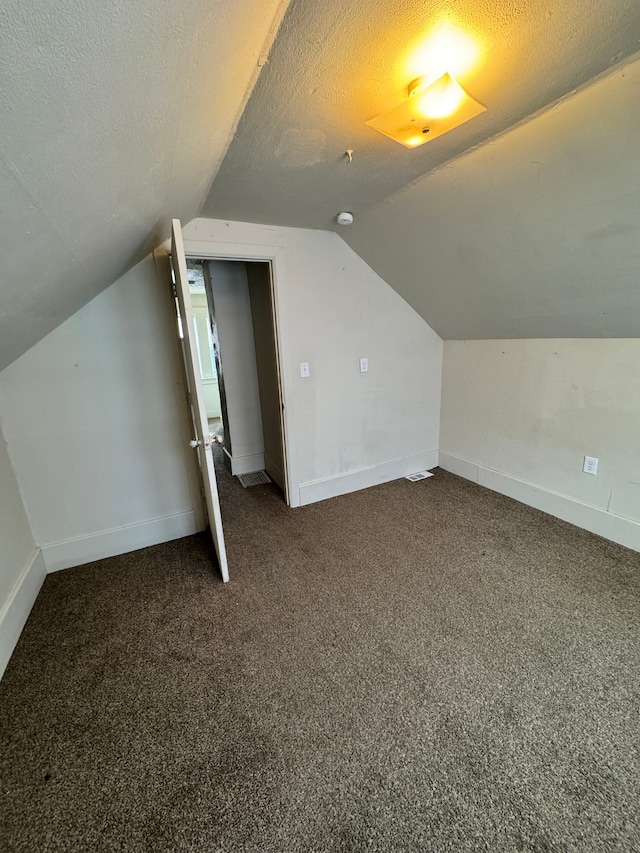 additional living space featuring a textured ceiling, dark colored carpet, lofted ceiling, and baseboards