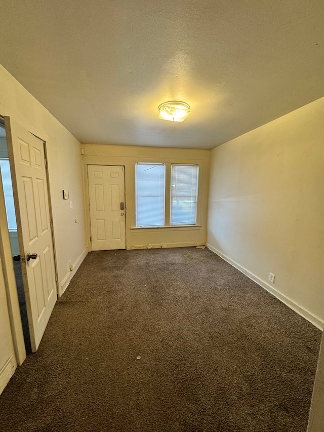 spare room featuring dark carpet, a textured ceiling, and baseboards