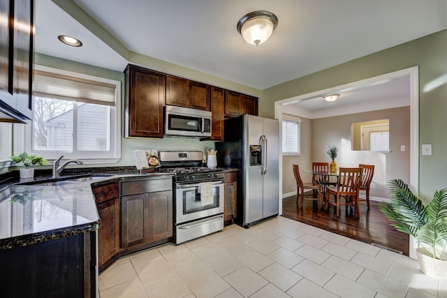 kitchen featuring dark brown cabinetry, stainless steel appliances, sink, and dark stone counters