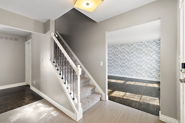 stairway featuring an accent wall, visible vents, baseboards, and wood finished floors