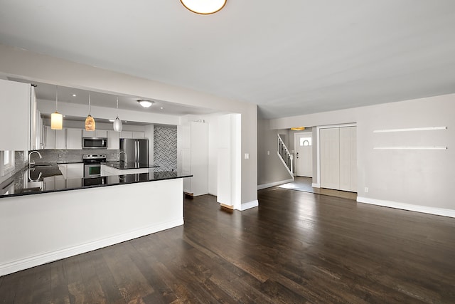 kitchen featuring dark wood finished floors, stainless steel appliances, dark countertops, tasteful backsplash, and a sink