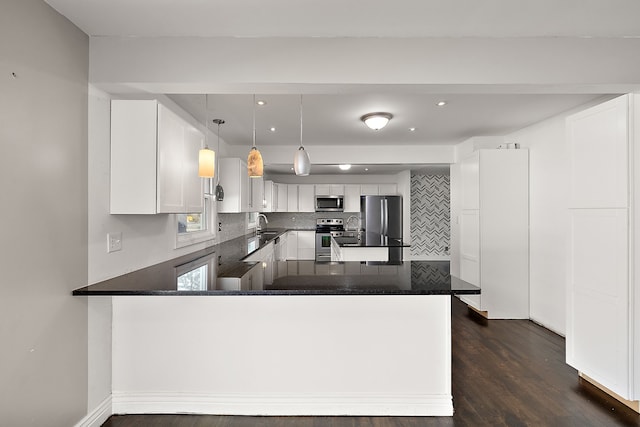 kitchen with dark wood-style flooring, stainless steel appliances, dark countertops, backsplash, and a peninsula