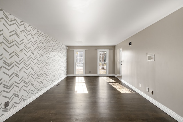 empty room featuring wallpapered walls, an accent wall, baseboards, and dark wood-type flooring