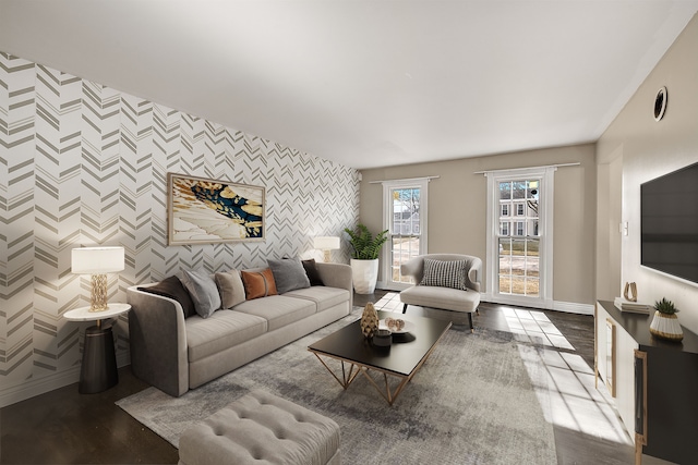 living room with wallpapered walls, an accent wall, baseboards, and wood finished floors