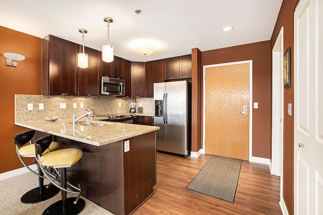 kitchen featuring appliances with stainless steel finishes, pendant lighting, sink, backsplash, and kitchen peninsula