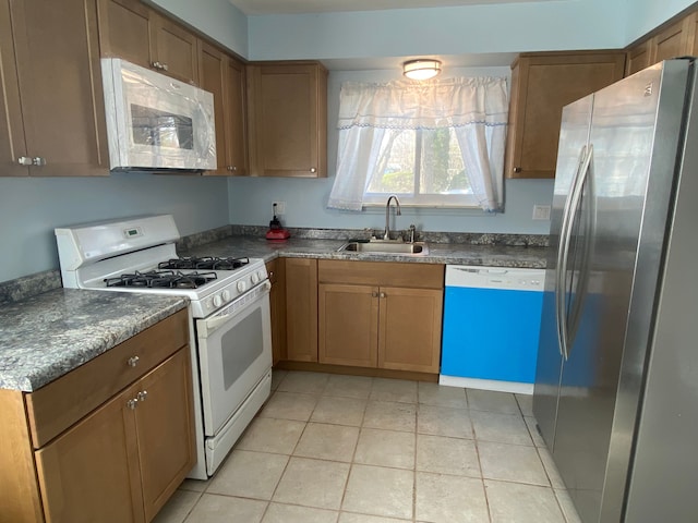 kitchen with light tile patterned flooring, sink, dark stone countertops, and white appliances