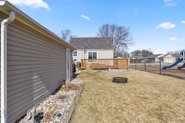 view of yard featuring a wooden deck, a playground, an outdoor fire pit, and fence