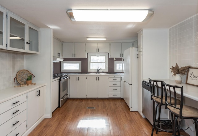 kitchen with sink, light hardwood / wood-style flooring, stainless steel appliances, decorative backsplash, and white cabinets