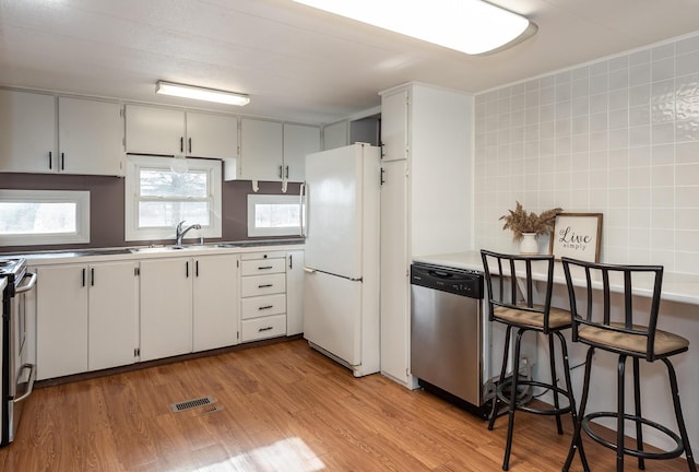 kitchen with sink, stainless steel appliances, light hardwood / wood-style floors, white cabinets, and decorative backsplash