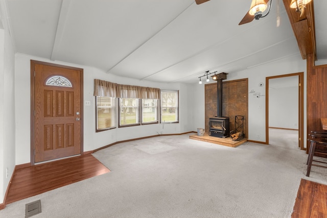 unfurnished living room featuring vaulted ceiling with beams, ceiling fan, carpet flooring, and a wood stove