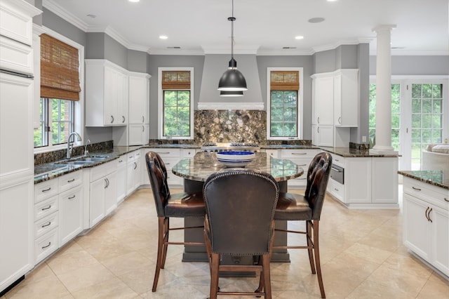 kitchen featuring white cabinets, decorative columns, backsplash, and a sink