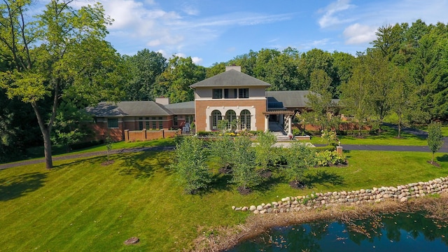 back of property with a lawn and a water view