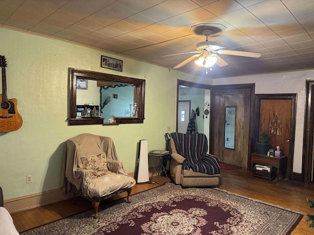 living area with a textured wall, wood finished floors, a ceiling fan, baseboards, and crown molding