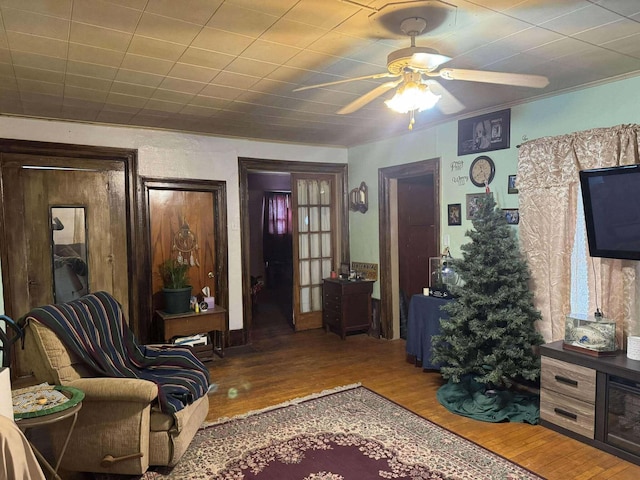 living area with ceiling fan, ornamental molding, and wood finished floors