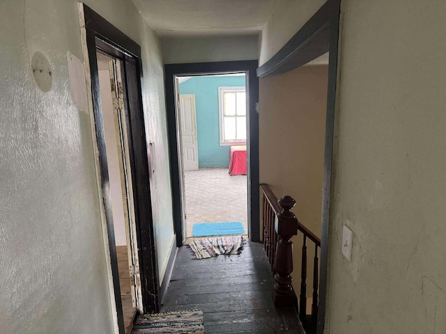 hall featuring a textured wall, hardwood / wood-style floors, and an upstairs landing