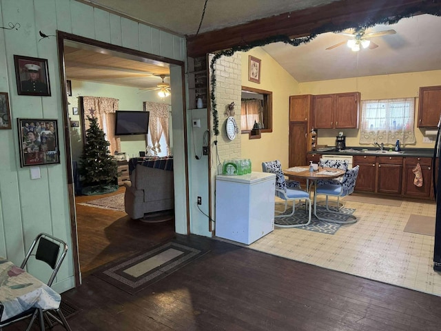 kitchen with a ceiling fan, dark countertops, vaulted ceiling, light wood-style floors, and a sink