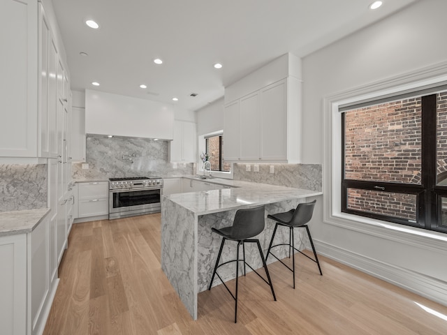 kitchen featuring white cabinetry, a kitchen bar, range with two ovens, light stone counters, and kitchen peninsula