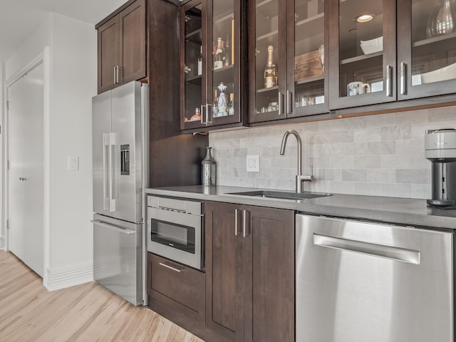 kitchen with appliances with stainless steel finishes, sink, dark brown cabinetry, and light hardwood / wood-style flooring