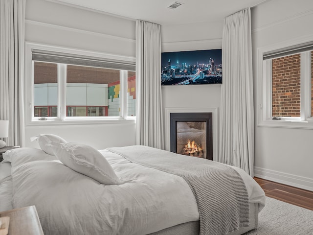 bedroom featuring multiple windows, a large fireplace, and hardwood / wood-style floors