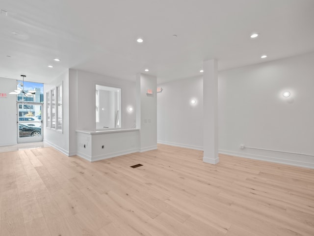 unfurnished living room featuring a notable chandelier and light hardwood / wood-style floors