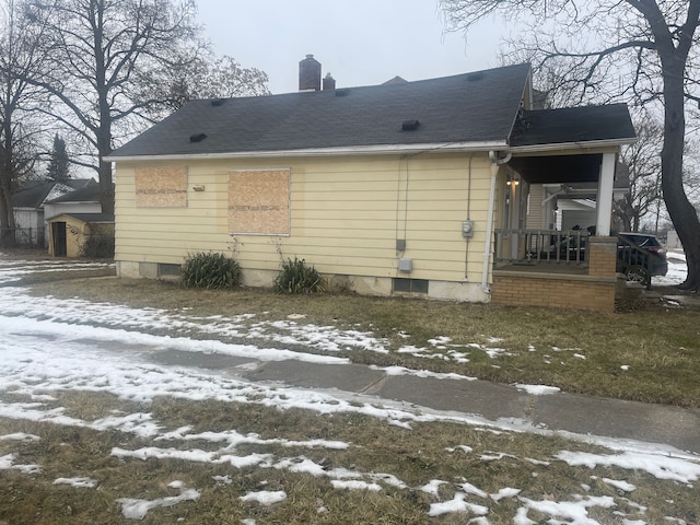 snow covered back of property featuring covered porch