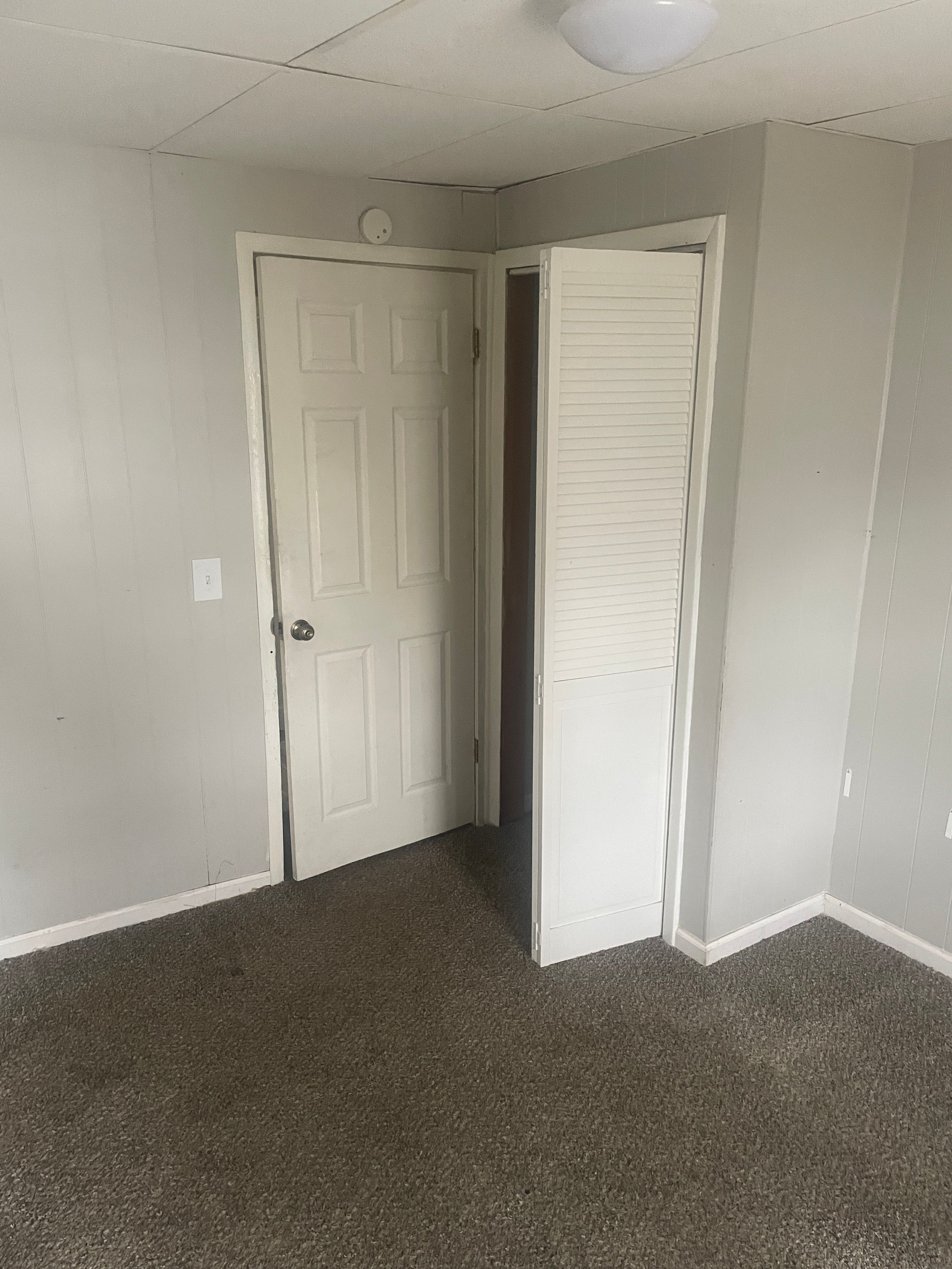 unfurnished bedroom with a paneled ceiling, dark carpet, and a closet