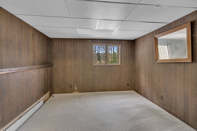 carpeted empty room with baseboard heating, a paneled ceiling, and wooden walls