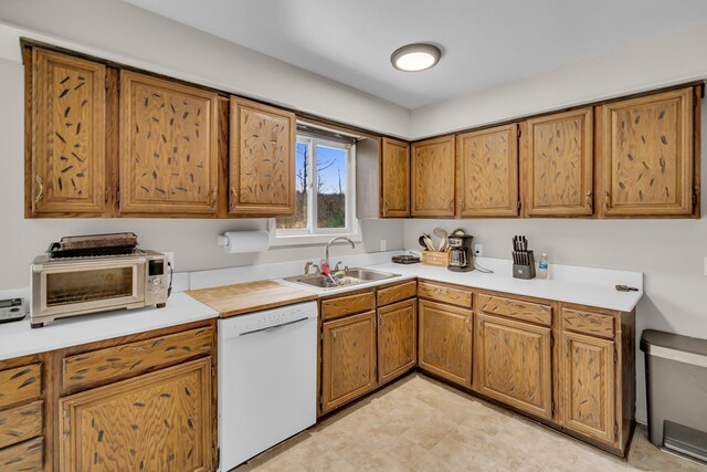 kitchen with a toaster, brown cabinets, light countertops, a sink, and dishwasher