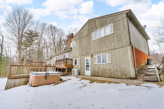 snow covered rear of property featuring a hot tub and a wooden deck