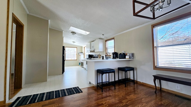 kitchen with a breakfast bar, lofted ceiling with skylight, ornamental molding, white cabinets, and kitchen peninsula