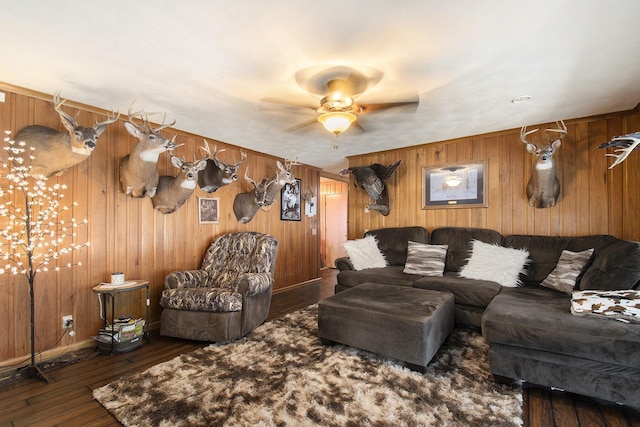 living room featuring dark wood-type flooring, ceiling fan, and wooden walls