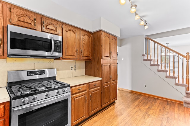 kitchen with appliances with stainless steel finishes, rail lighting, and light hardwood / wood-style flooring