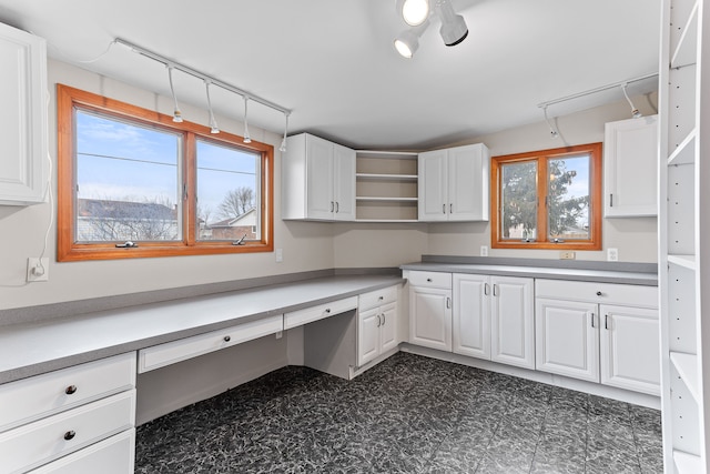 kitchen featuring rail lighting, built in desk, and white cabinets