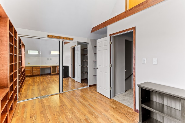 unfurnished bedroom featuring built in desk, light wood-type flooring, and two closets