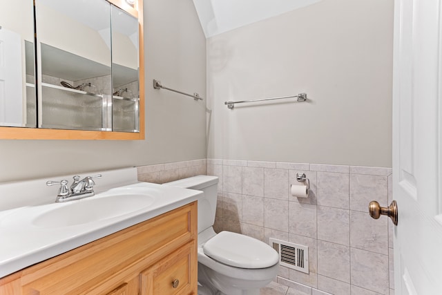 bathroom with vanity, toilet, a shower with door, and tile walls