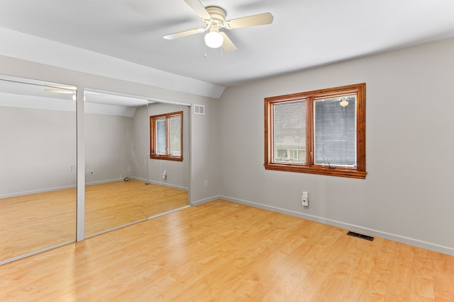 unfurnished bedroom featuring ceiling fan, light hardwood / wood-style flooring, and two closets